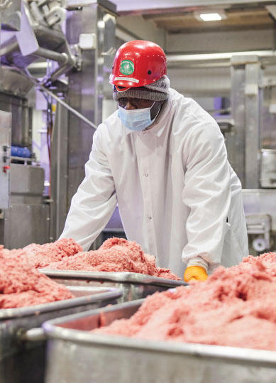worker in lab coat processing raw meat